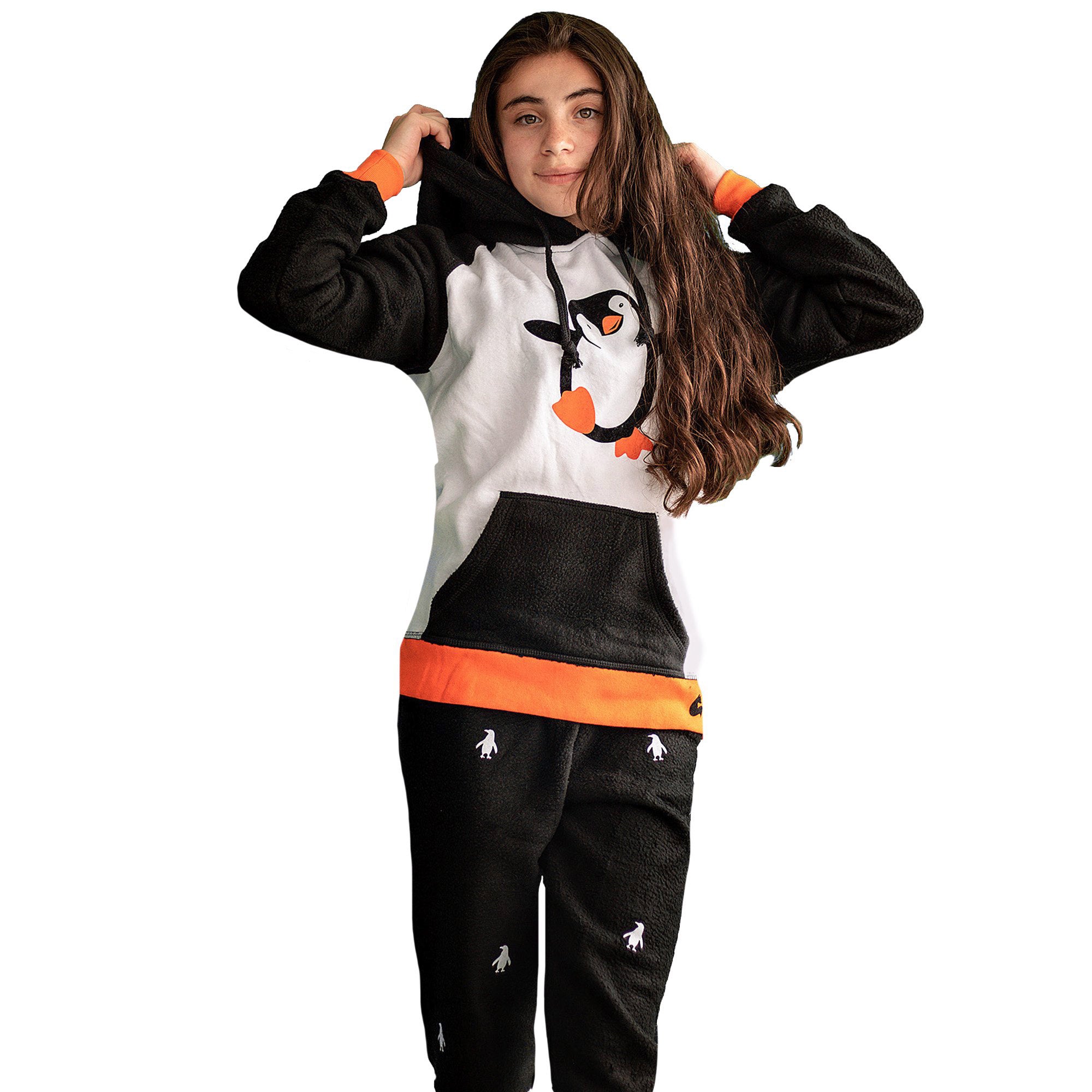 Niña de frente vistiendo la Pijama Pingüino negra y blanco con ribs naranja y capota negra con un lindo pingüino bailando en el pecho, diseño de Arctic Fox Colombia