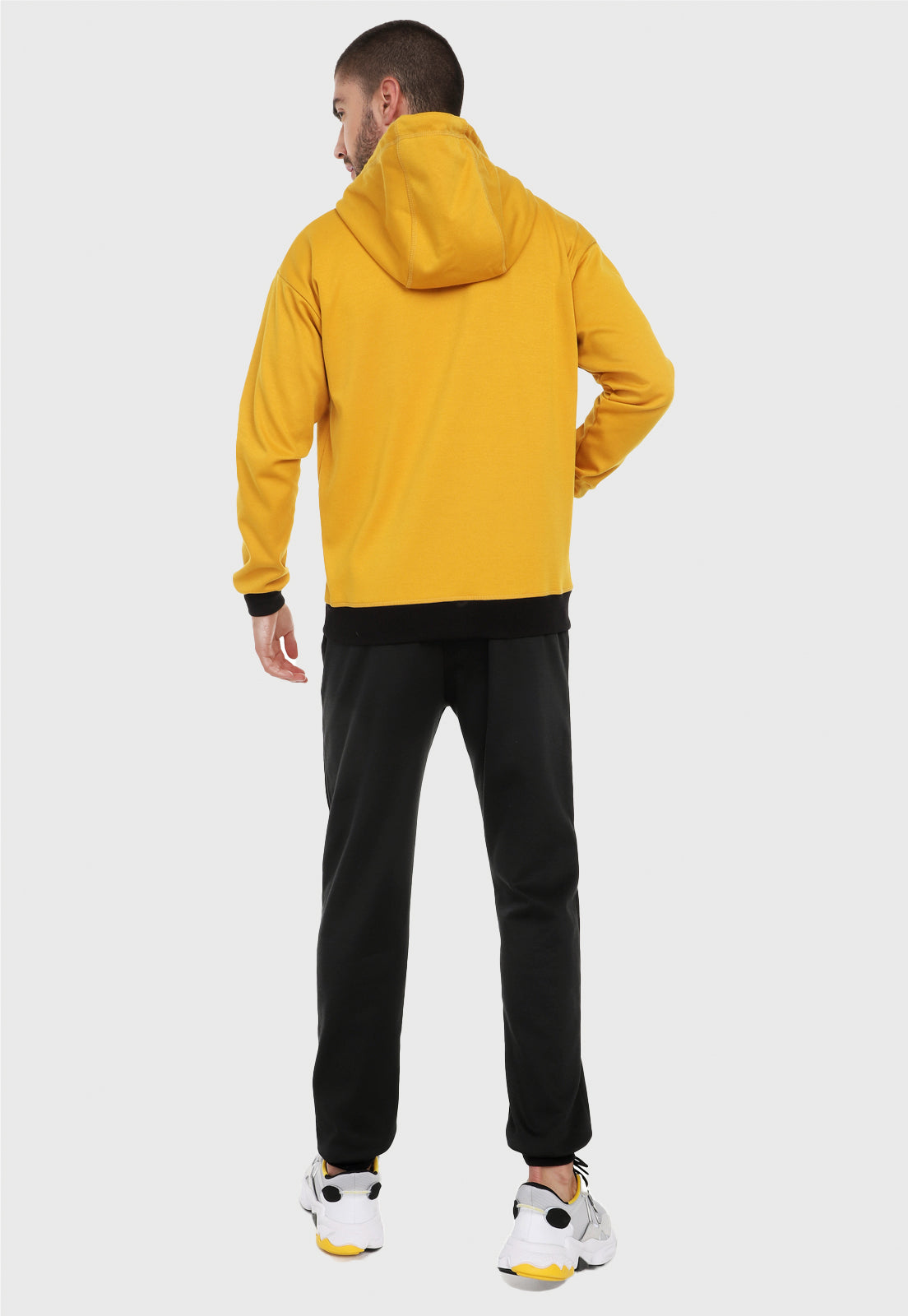 Hombre adulto visto de espalda vistiendo la sudadera para hombre conjunto chaqueta hoodie mostaza con pantalón de sudadera negro.