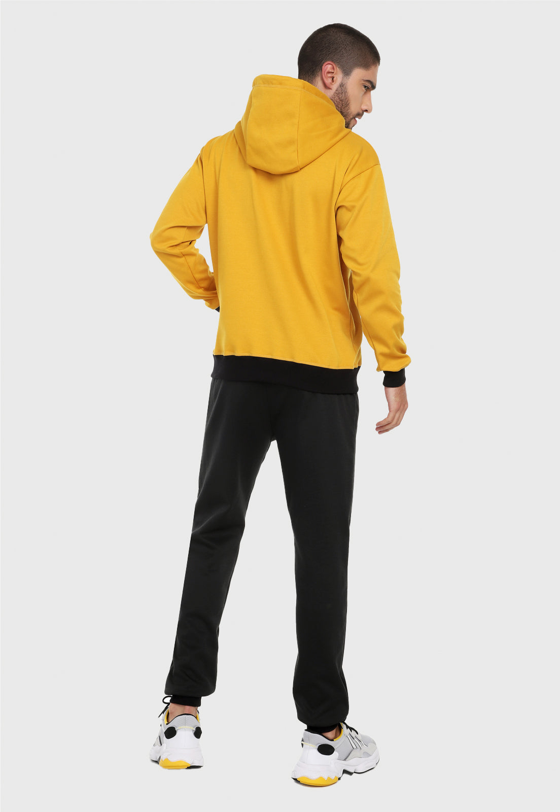 Hombre adulto visto de espalda vistiendo la sudadera para hombre conjunto buzo hoodie Mostaza y Negro con pantalón de sudadera negro.
