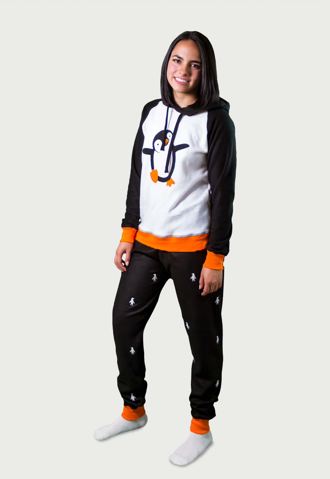 Mujer vistiendo la Pijama para Mujer referencia pingüino con siluetas de pingüino blancas estampadas en el pantalón. La pijama es de color negro, blanco y naranja con el pingüino bailarín estampado en el pecho, diseño de Arctic Fox Colombi