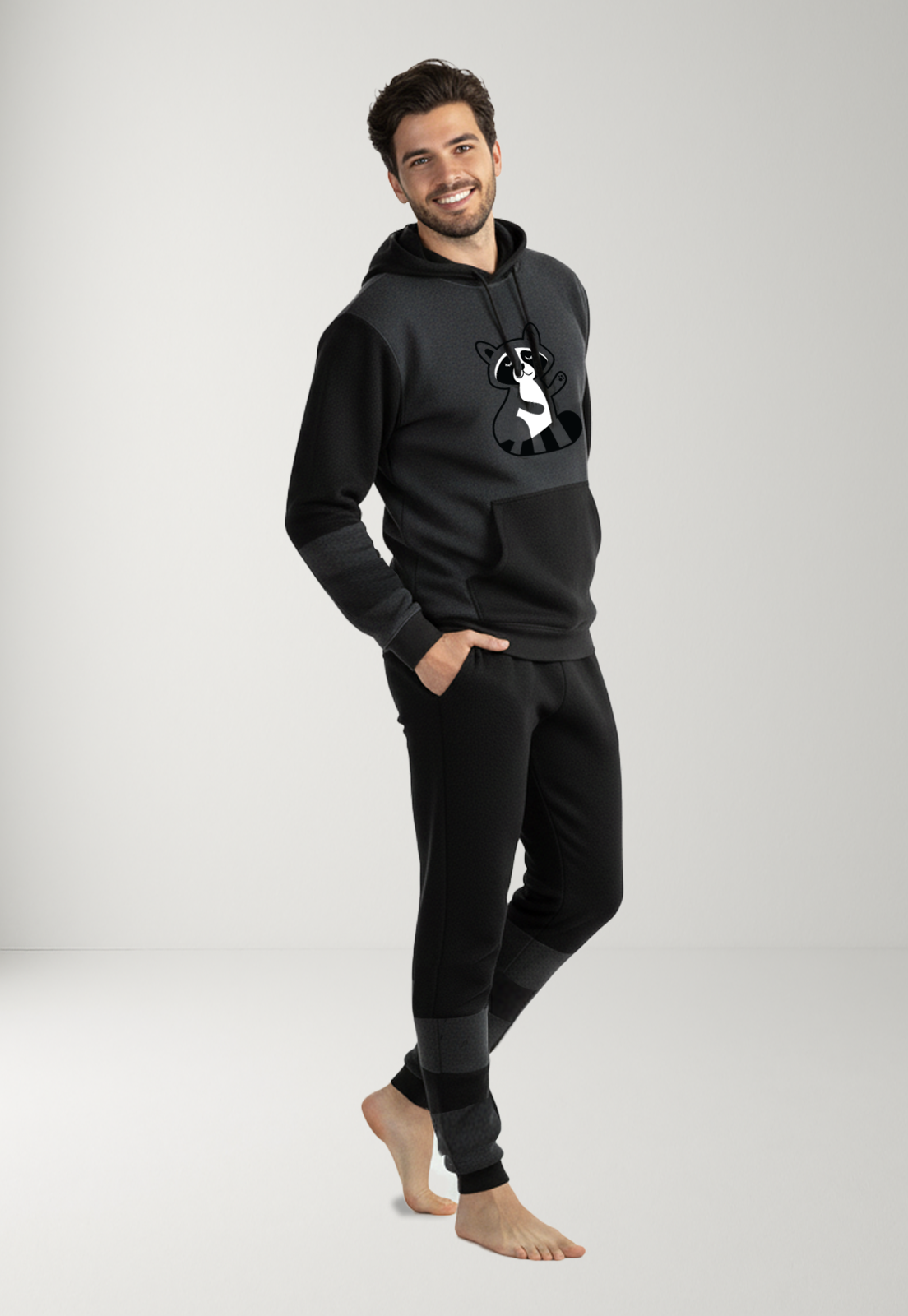 hombre usando una pijama gris con negro con capota, tiene un mapache estampado en el frente 