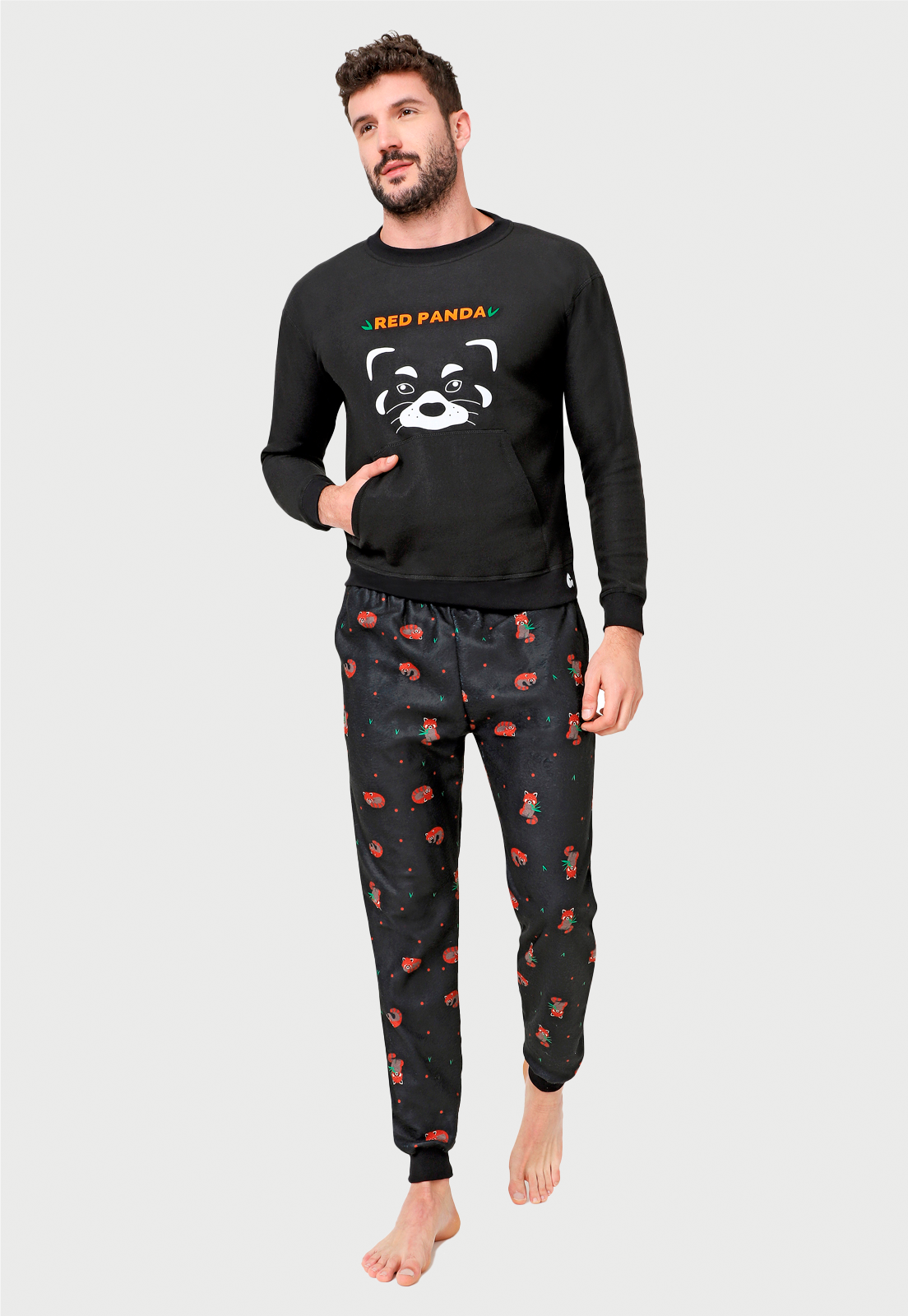 Hombre joven luciendo una pijama con un dibujo de panda rojo en el saco y un pantalon estampado con muchos pandas  rojos comiendo banboo