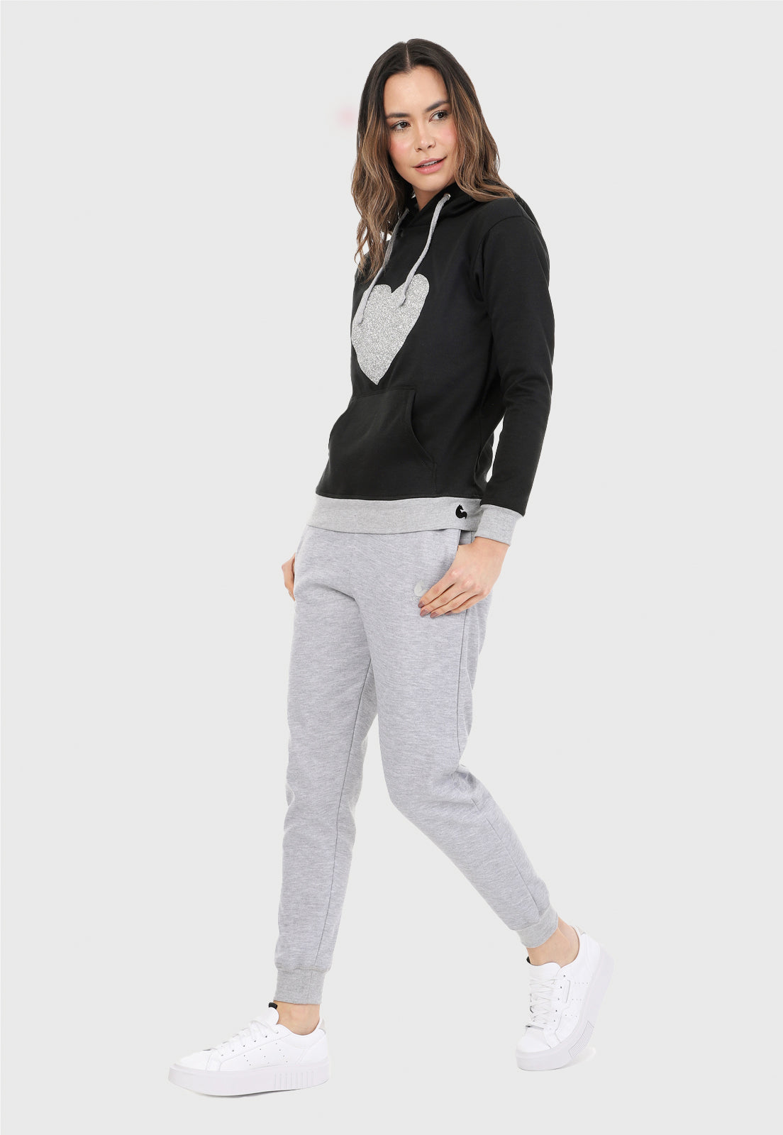 Mujer vistiendo la sudadera para mujer buzo hoodie negro con corazón brillante y pantalón de sudadera gris.