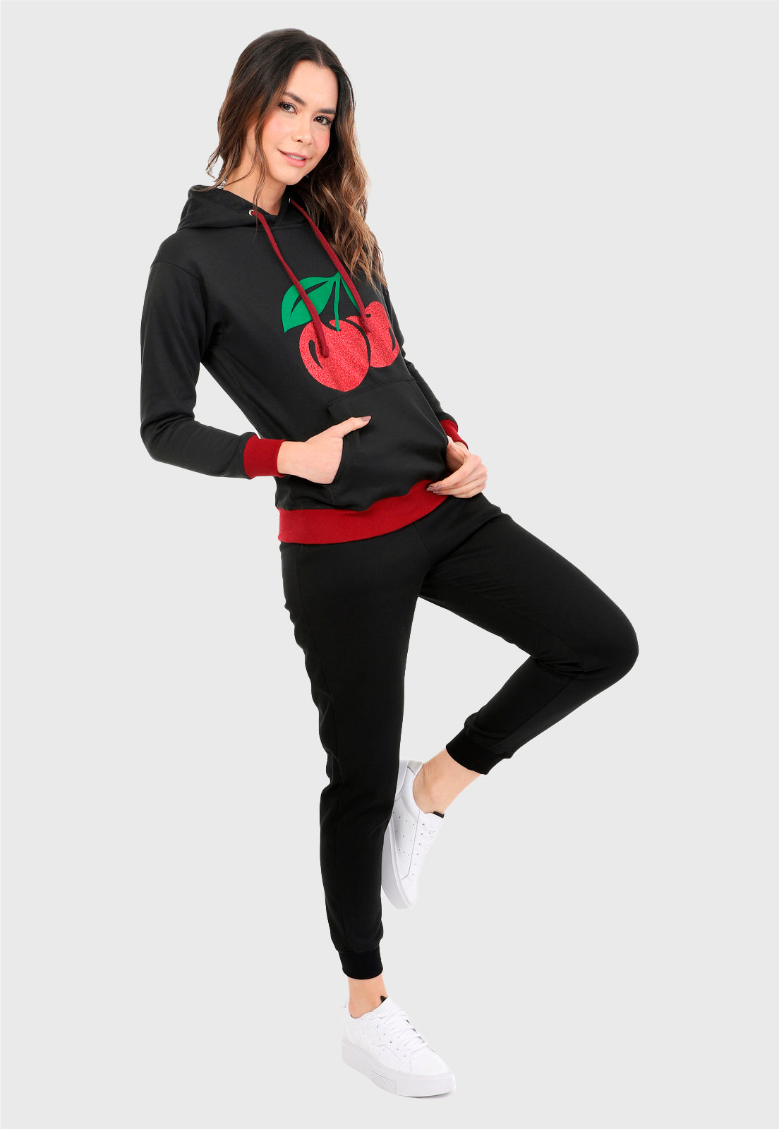 Mujer vistiendo la sudadera para mujer conjunto buzo hoodie negro con cerezas brillantes, ribs vinotinto en puño y cintura y pantalón de sudadera negro.