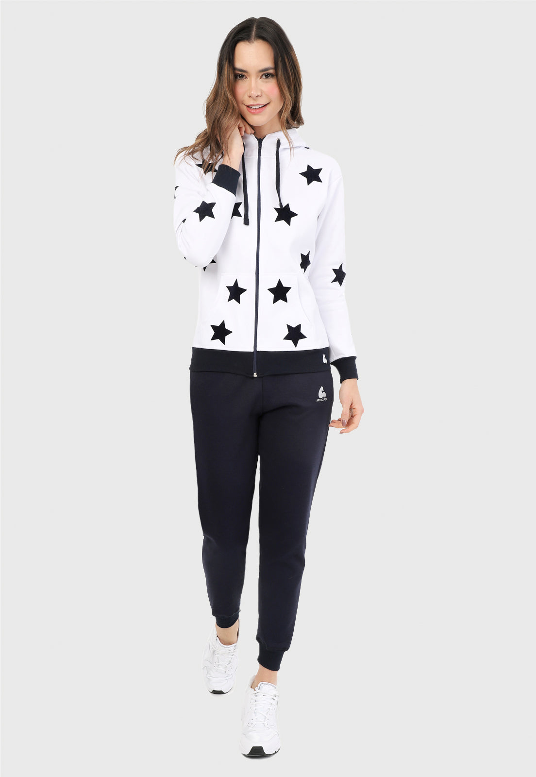 Mujer vistiendo la sudadera para mujer conjunto chaqueta hoodie blanca con estrellas azules estampadas en terciopelo y pantalón de sudadera azul.