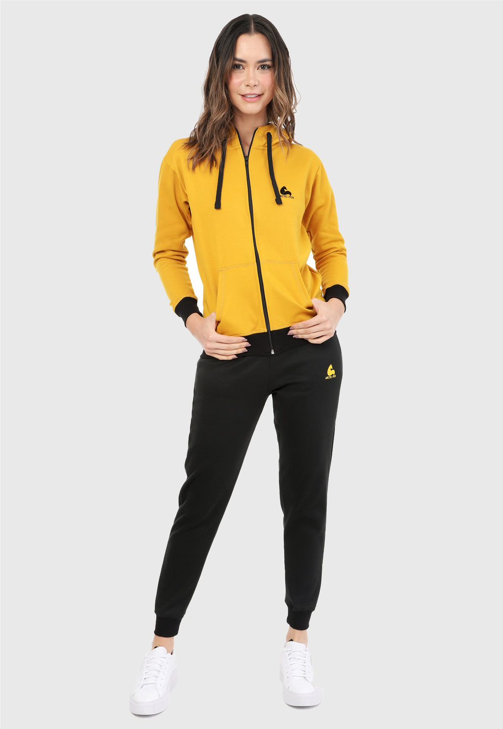 Mujer vistiendo la sudadera para mujer conjunto chaqueta hoodie color mostaza y pantalón de sudadera negro.