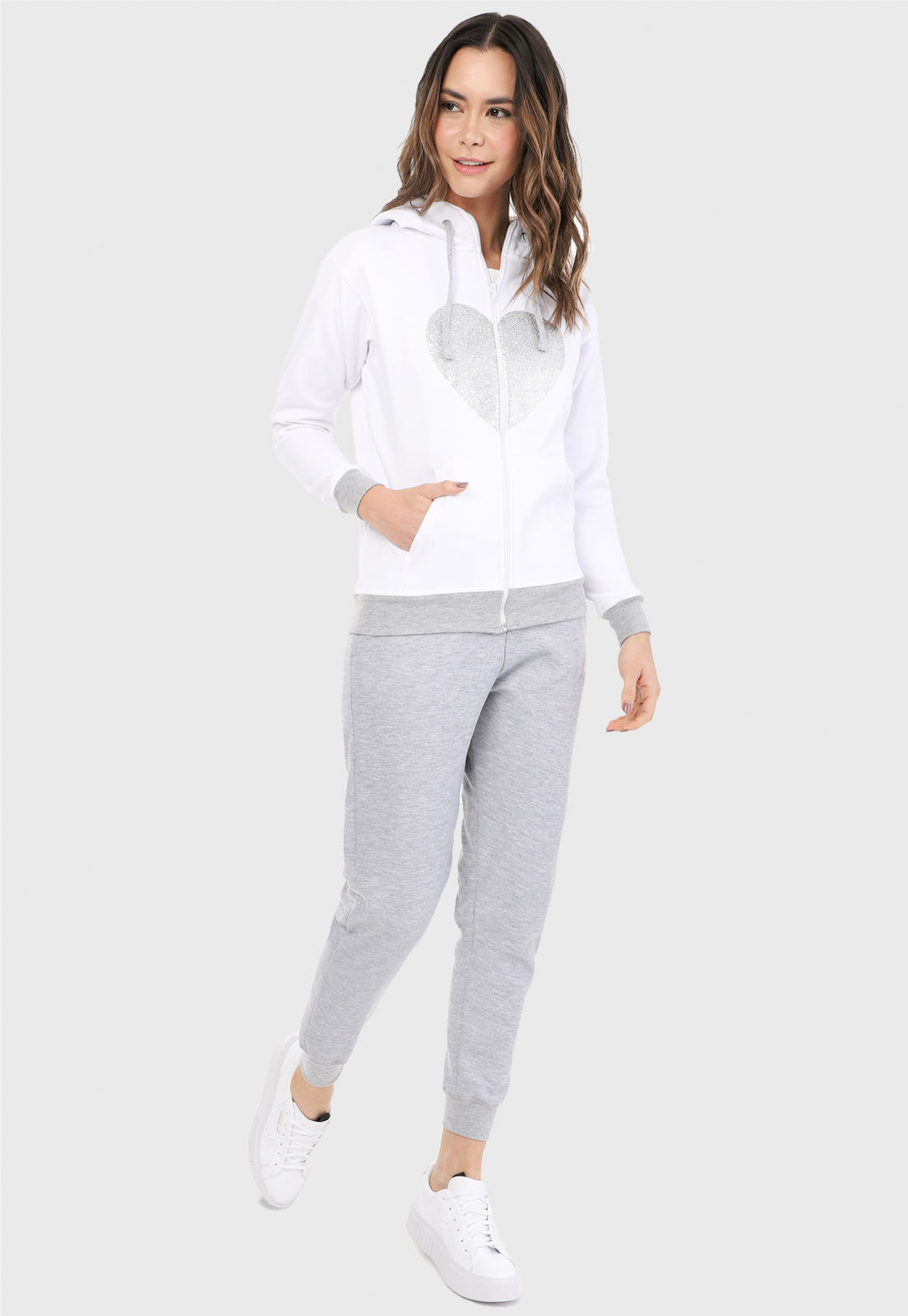 Mujer vistiendo la sudadera para mujer conjunto chaqueta hoodie blanco y gris con corazón brillante y pantalón de sudadera gris.
