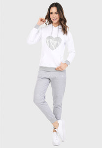 Mujer vistiendo la sudadera para mujer conjunto buzo hoodie color blanco con corazón plateado y pantalón de sudadera gris.