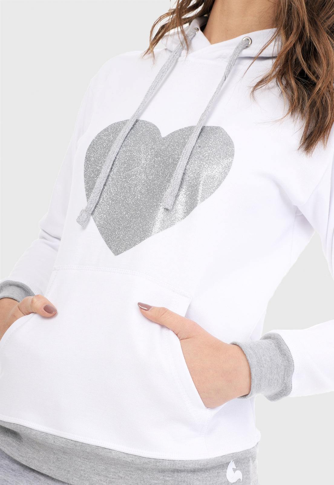 Detalle de Mujer vistiendo la sudadera para mujer conjunto buzo hoodie color blanco con corazón plateado y pantalón de sudadera gris.