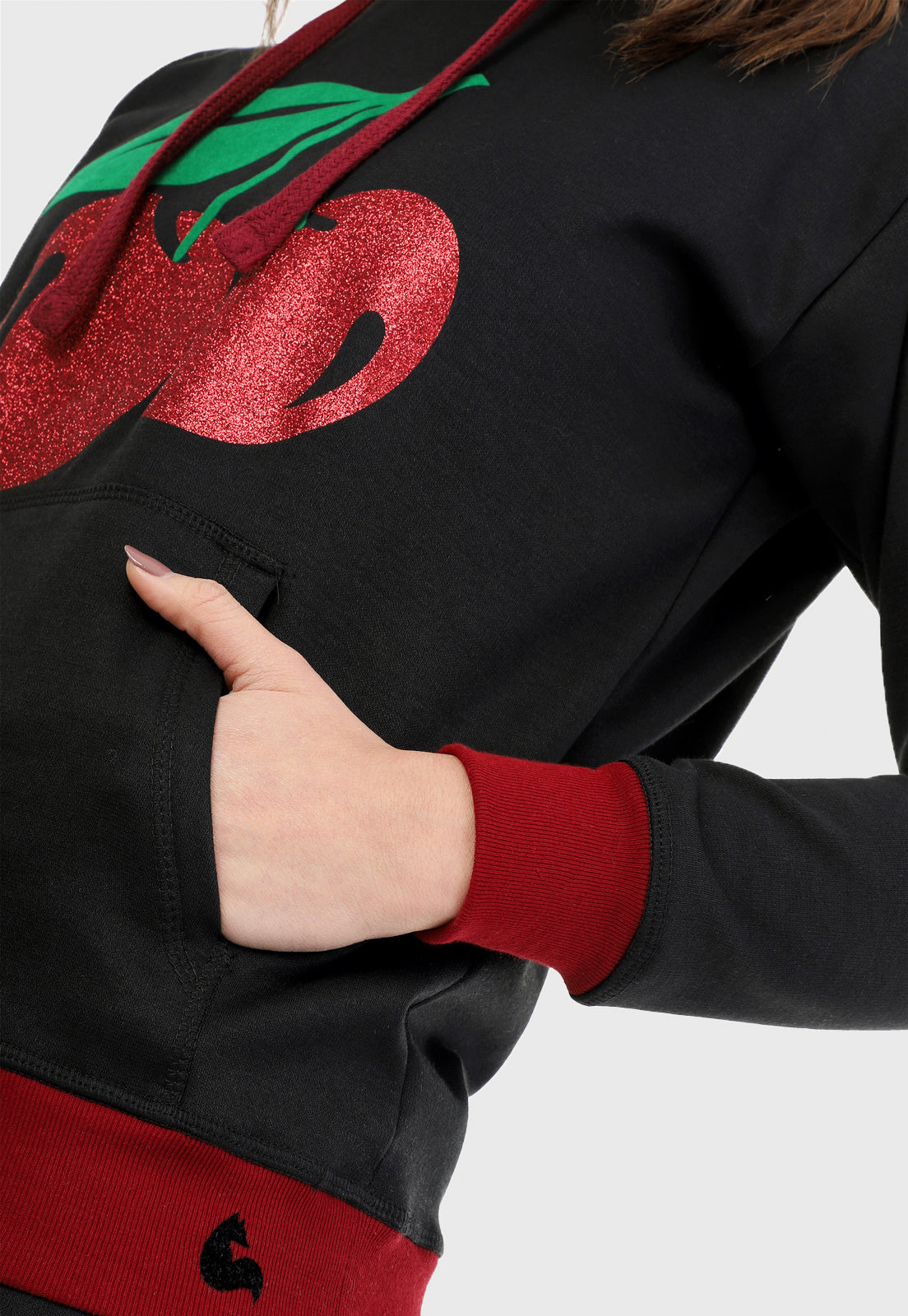 Detalle de mujer vistiendo la sudadera para mujer conjunto buzo hoodie negro con cerezas brillantes, ribs vinotinto en puño y cintura y pantalón de sudadera negro.