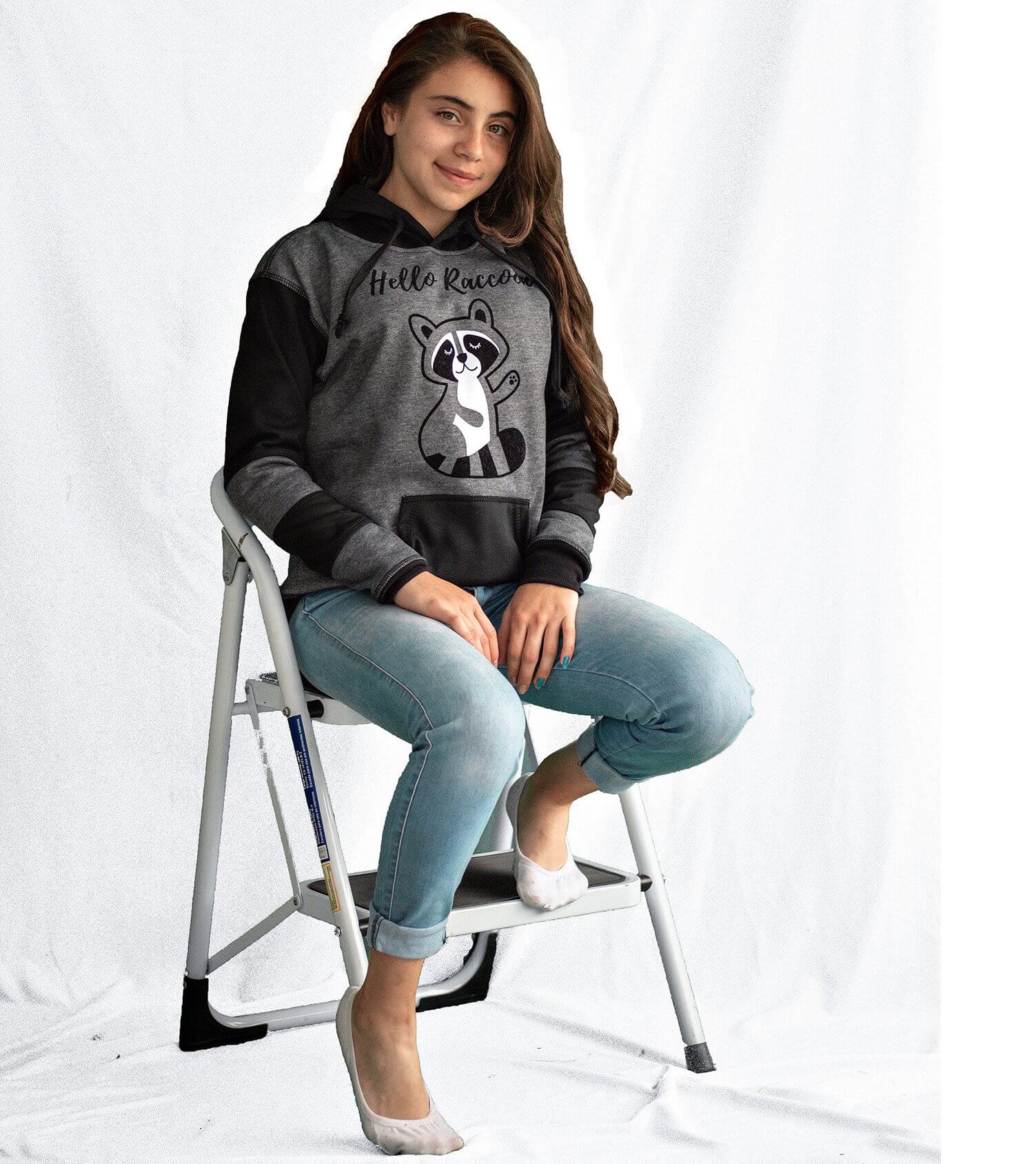Niña vistiendo el Buzo Hoodie Gris y Negro con Mapache estampado en el pecho y franjas negras en las mangas.