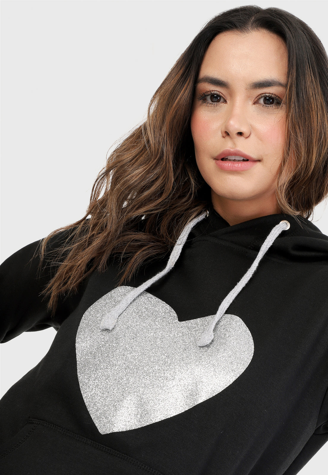 Detalle de Mujer vistiendo la sudadera para mujer buzo hoodie negro con corazón brillante y pantalón de sudadera gris.