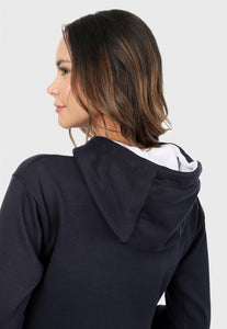 Detalle mujer de espalda vistiendo la sudadera para mujer conjunto buzo hoodie azul navy con capota forrada en blanco y pantalón de sudadera gris jaspe.