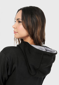Detalle de Mujer vista de espalda vistiendo la sudadera para mujer buzo hoodie negro con corazón brillante y pantalón de sudadera gris.