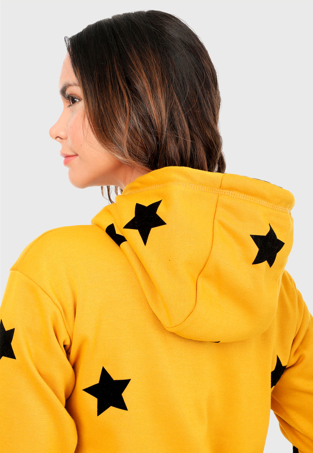 Detalle de Mujer vista de espalda vistiendo la sudadera para mujer conjunto buzo hoodie color mostaza con estrellas estampadas en negro y pantalón de sudadera negro.