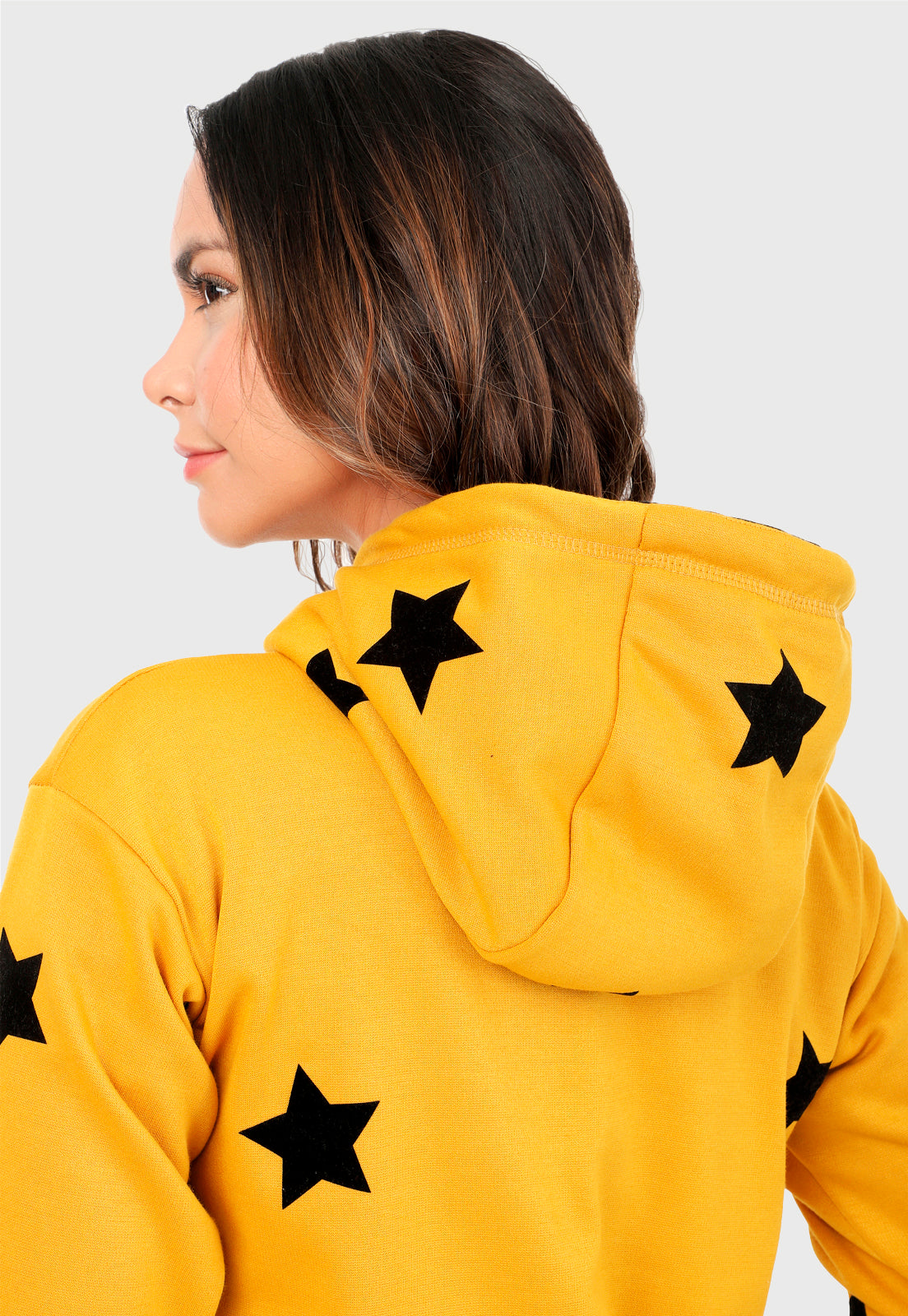 Detalle de Mujer vista de espalda vistiendo la sudadera para mujer conjunto buzo hoodie color mostaza con estrellas estampadas en negro y pantalón de sudadera negro.