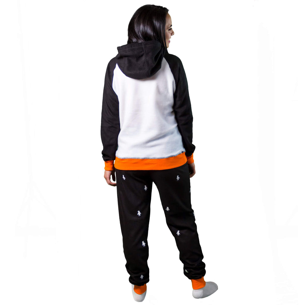 Mujer de espalda vistiendo la Pijama para Mujer referencia pingüino con siluetas de pingüino blancas estampadas en el pantalón. La pijama es de color negro, blanco y naranja con el pingüino bailarín estampado en el pecho, diseño de Arctic Fox Colombia
