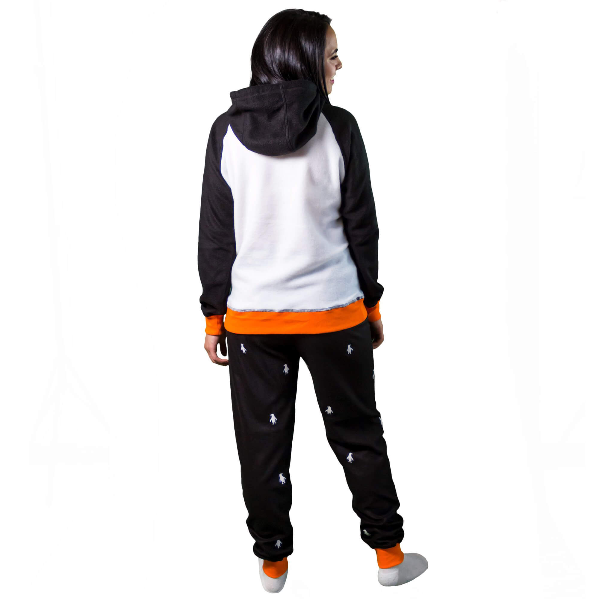Mujer de espalda vistiendo la Pijama para Mujer referencia pingüino con siluetas de pingüino blancas estampadas en el pantalón. La pijama es de color negro, blanco y naranja con el pingüino bailarín estampado en el pecho, diseño de Arctic Fox Colombia