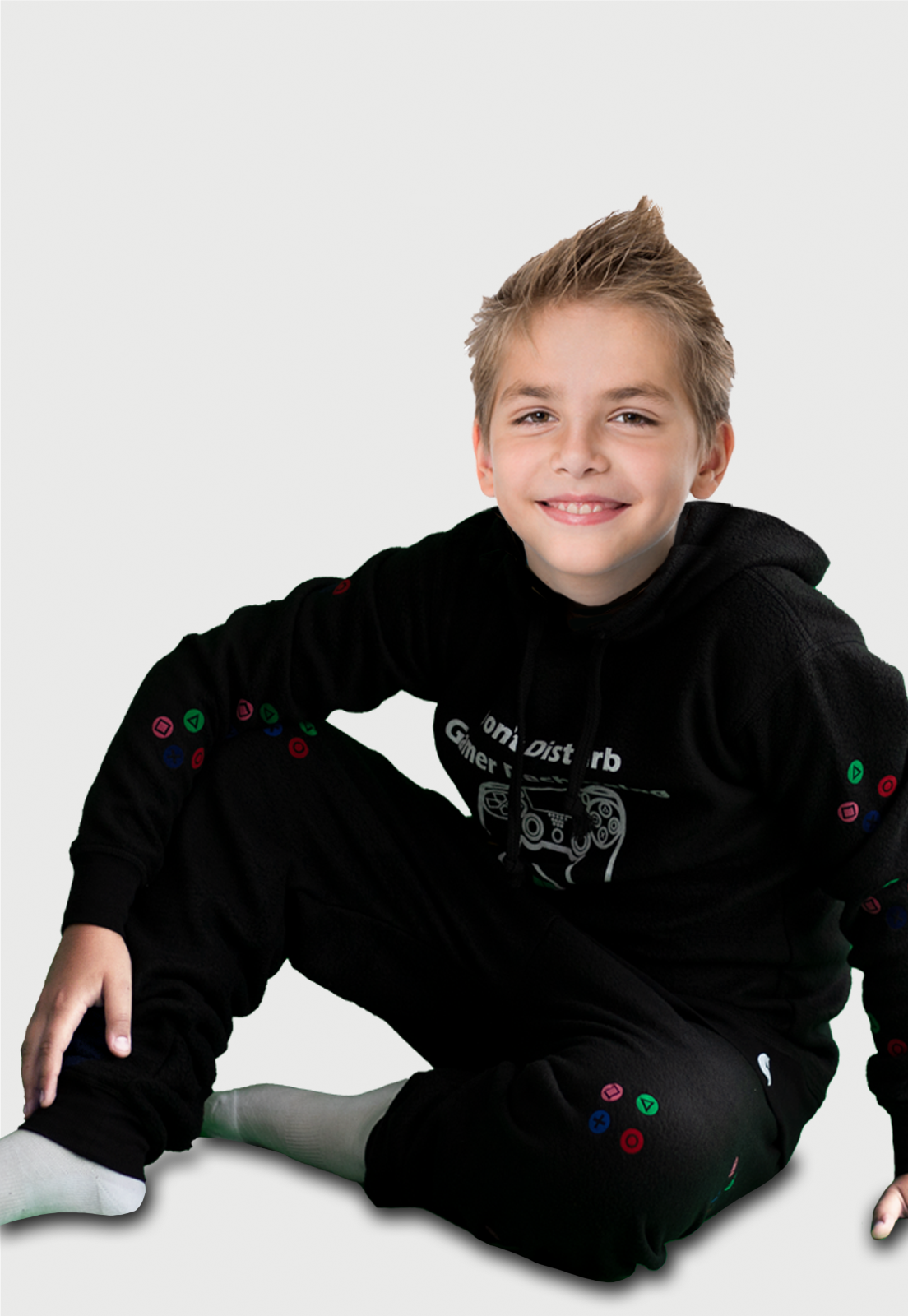 Niño sentado vistiendo la Pijama para Niño Negra referencia Gamer Play con un control de gamer y el icono de batería cargando estampado en el pecho, en las mangas de pantalón y buzo van estampados los comando de juego en diferentes colores, diseño de Arctic Fox Colombia