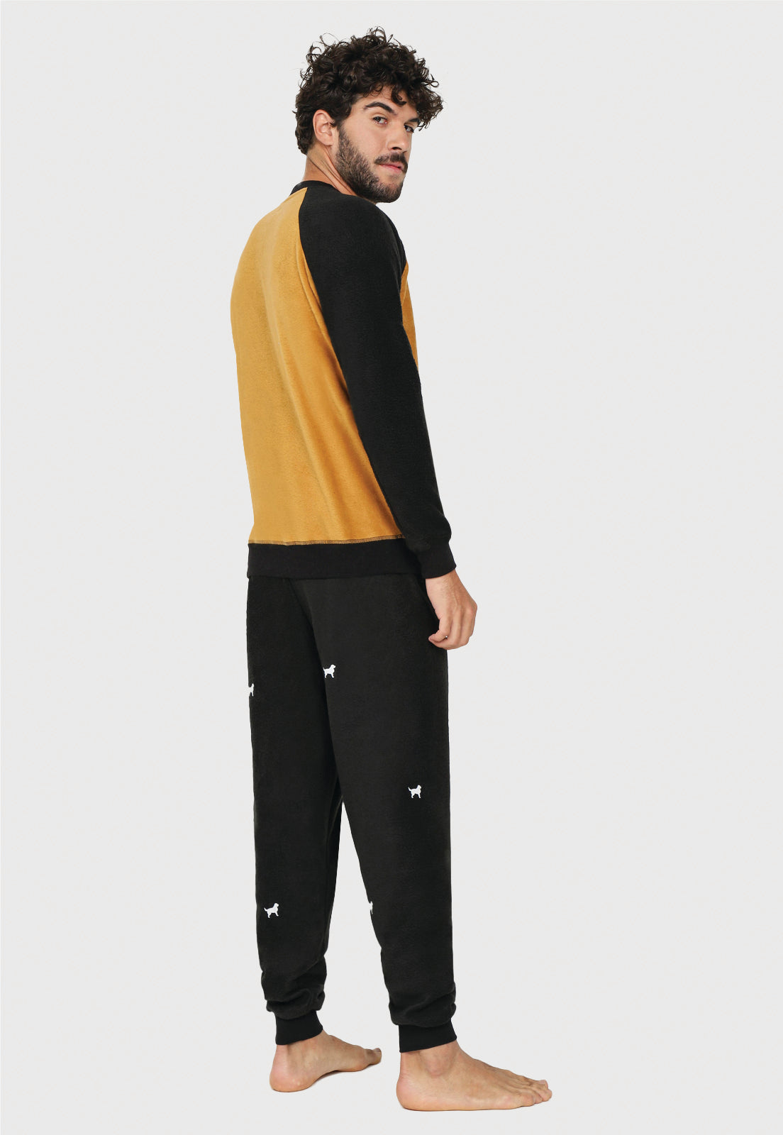 joven de medio lado luciendo una pijama de dos colores el pantalon negro tiene siluetas blancas de bernes de la montaña