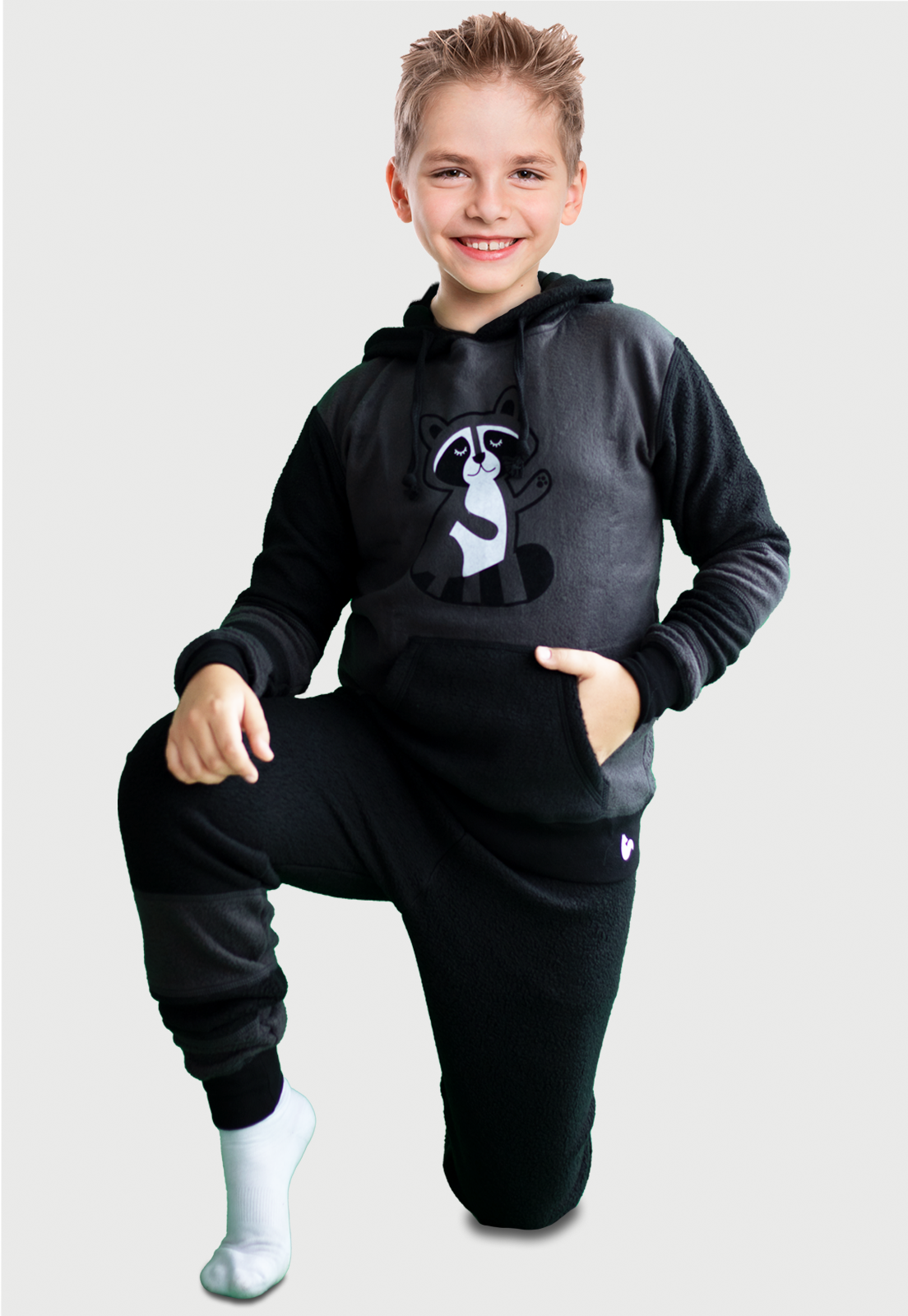 Lindo Niño cuerpo entero arrodillado en el piso vistiendo la Pijama Mapache negra y gris con un lindo mapache estampado en el pecho, diseño de Arctic Fox Colombia