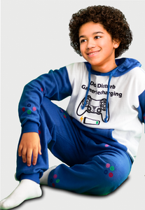 Niño sentado con una pijama tipo sudadera blanca con azul rey con un control remoto de gamer en el saco y el pantalón botones de colores