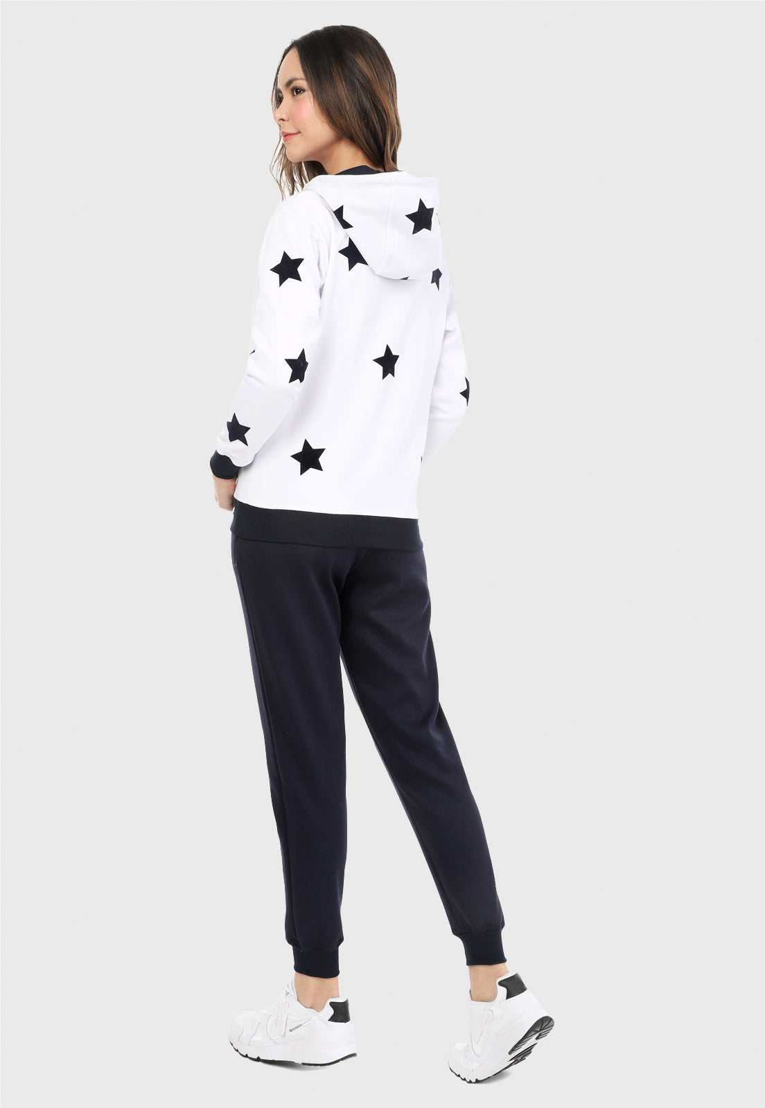 Mujer de espalda vistiendo la sudadera para mujer conjunto chaqueta hoodie blanca con estrellas azules estampadas en terciopelo y pantalón de sudadera azul.