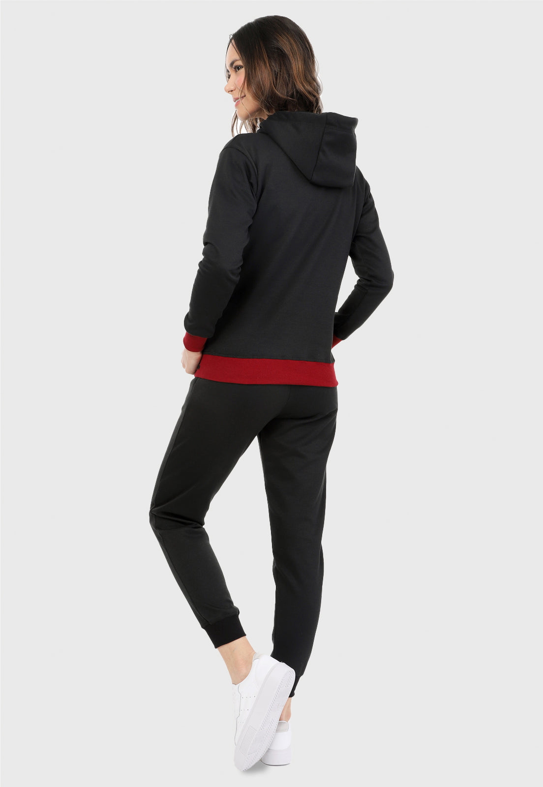 Mujer vista de espalda vistiendo la sudadera para mujer conjunto buzo hoodie negro con cerezas brillantes, ribs vinotinto en puño y cintura y pantalón de sudadera negro.