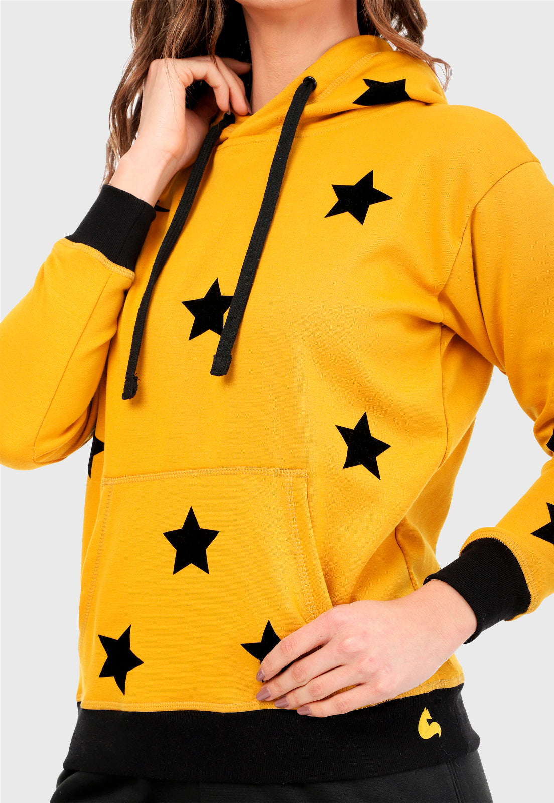 Detalle de mujer vistiendo la sudadera para mujer conjunto buzo hoodie color mostaza con estrellas estampadas en negro y pantalón de sudadera negro.