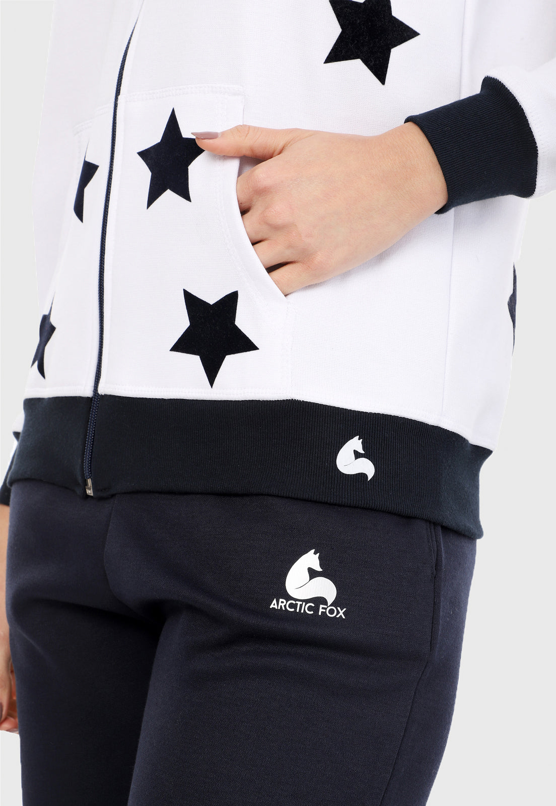 Detalle en bolsillo de mujer vistiendo la sudadera para mujer conjunto chaqueta hoodie blanca con estrellas azules estampadas en terciopelo y pantalón de sudadera azul.