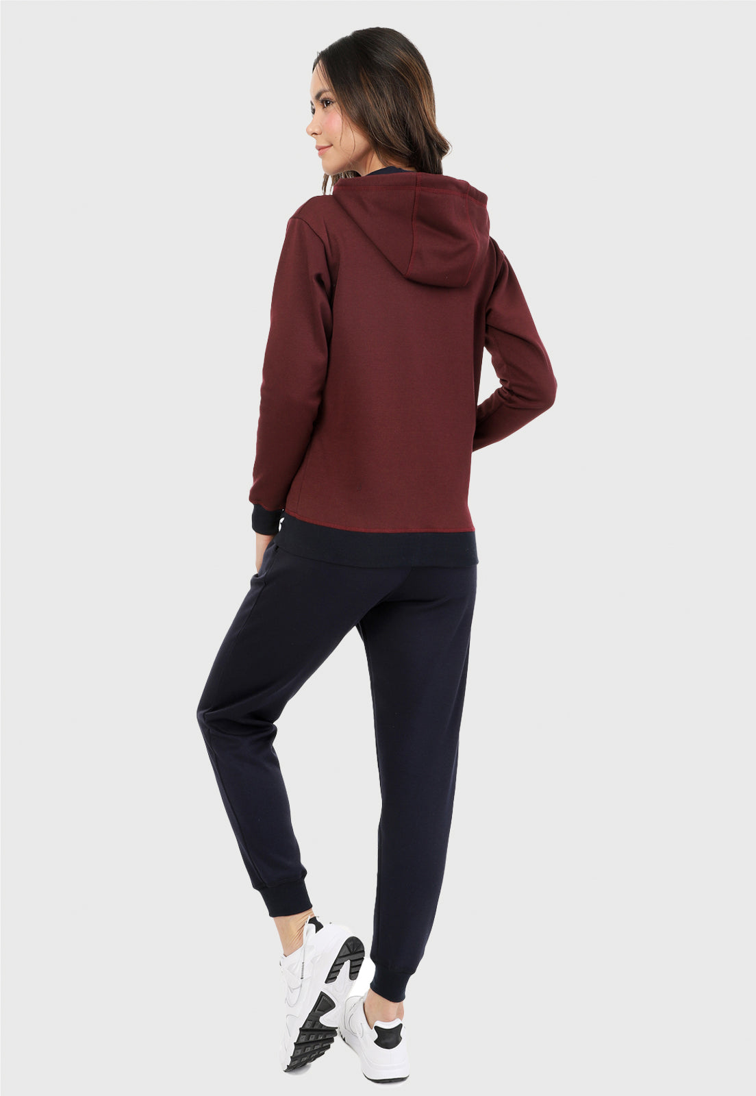 Mujer vista de espalda vistiendo la sudadera para mujer conjunto chaqueta hoodie vinotinto con capota forrada en azul al interior y pantalón de sudadera azul.