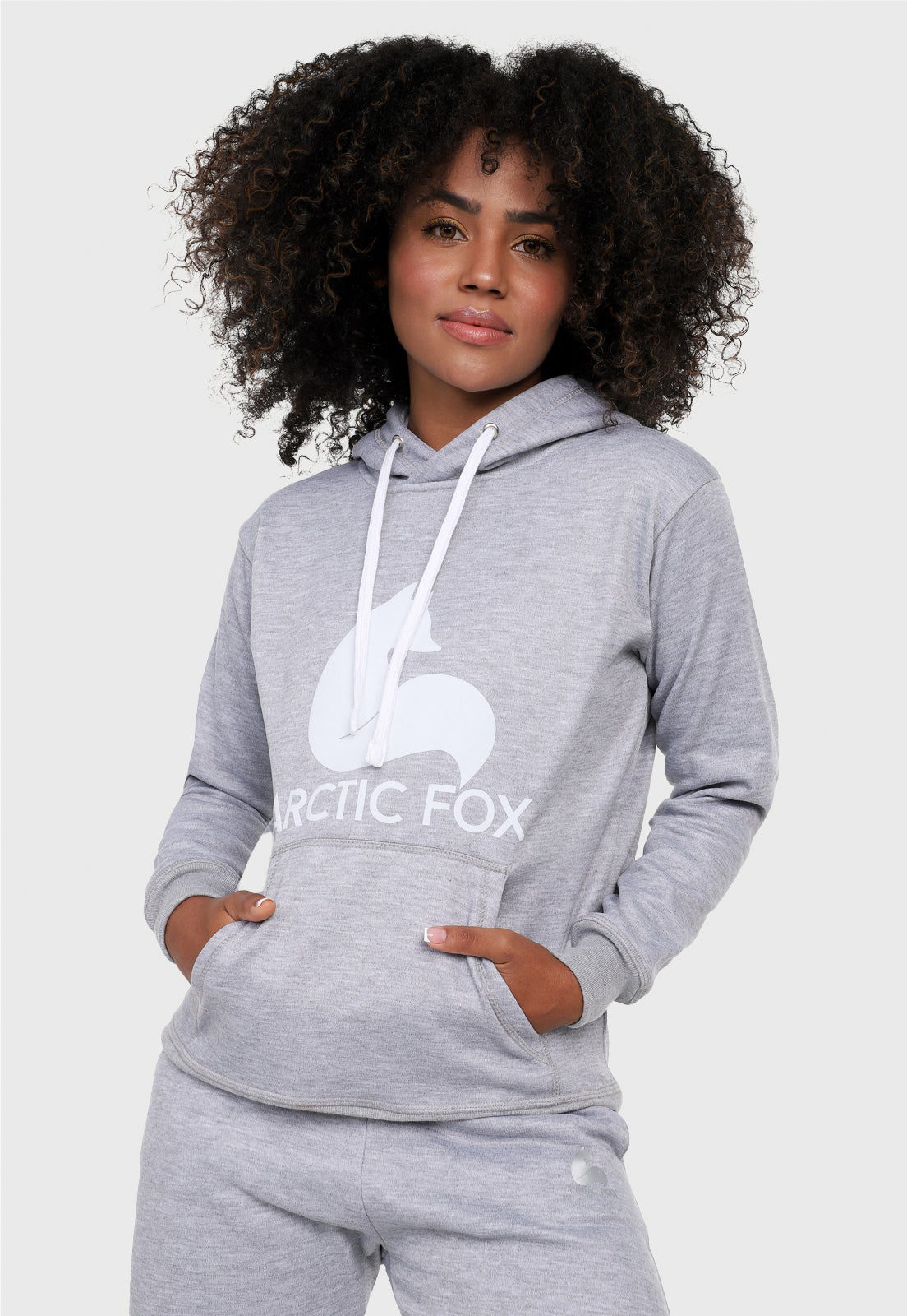 Detalle de mujer vistiendo la sudadera para mujer conjunto buzo hoodie y pantalón de sudadera gris jaspe. Lleva el zorro de Arctic Fox estampado en blanco al frente del buzo.