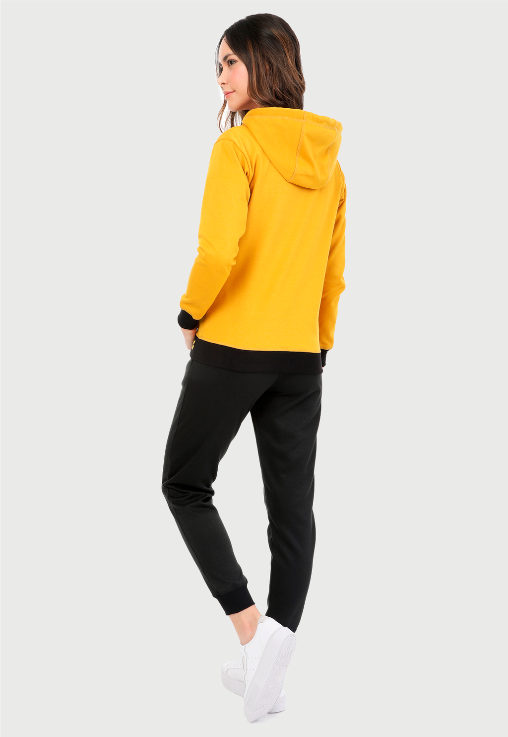 Mujer vistiendo la sudadera para mujer conjunto chaqueta hoodie color mostaza y pantalón de sudadera negro.