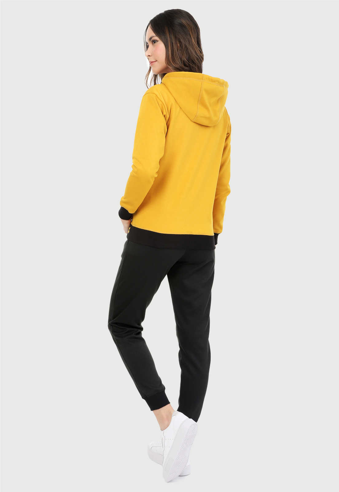 Mujer vistiendo la sudadera para mujer conjunto chaqueta hoodie color mostaza y pantalón de sudadera negro.