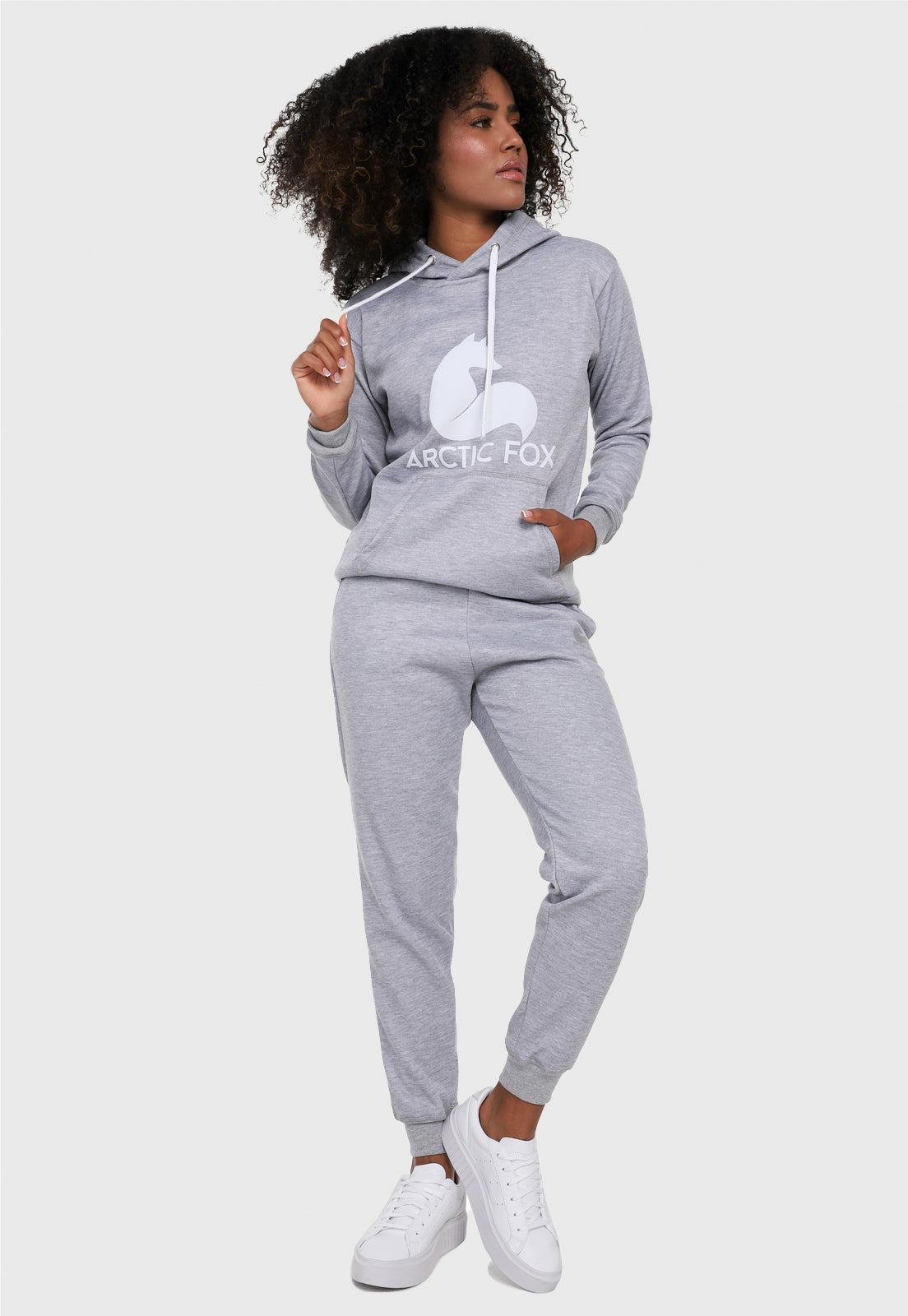 Mujer vistiendo la sudadera para mujer conjunto buzo hoodie y pantalón de sudadera gris jaspe. Lleva el zorro de Arctic Fox estampado en blanco al frente del buzo.